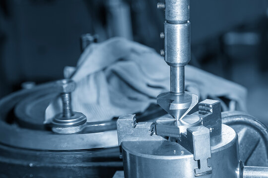 Close-up of a manual hole chamfering process on precision metal parts using a hand deburring tool in a blue-toned workshop.