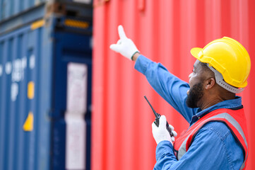 African American container operators wearing yellow helmets and safety vests control via walkie-talkie workers in container yards. Transportation import and export logistic industry concept.
