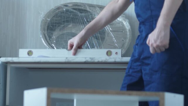 Furniture assembly specialist using tape measure and spirit level to measure a kitchen cabinet. Worker in uniform preparing the base for kitchen sink and countertop installation.