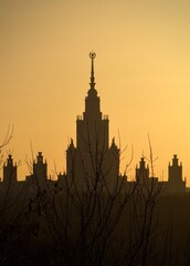 Naklejka premium Silhouette of the main building of Moscow State University in Moscow, Russia, set against a warm sunset sky with its recognizable spire and monumental outline.
