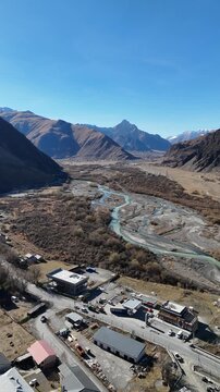erial cinematic view of Stepantsminda village in Kazbegi, Georgia, surrounded by Caucasus Mountains - Vertical drone shot.