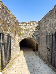 Fototapeta premium Stone tunnel entrance at Old Fortress in Corfu Old Town, Greece. Iron gates and paved walkway leading inside, blue sky