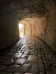 Fototapeta premium Stone tunnel passage inside the Old Fortress in Corfu Old Town, Greece. A bright exit over cobblestone path