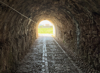 Fototapeta premium Stone tunnel and cobblestone path inside Corfu island New Fortress, Greece. Bright day light at the exit
