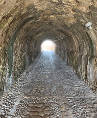 Fototapeta premium Stone tunnel and cobblestone path inside Corfu island New Fortress, Greece. Bright day light at the exit
