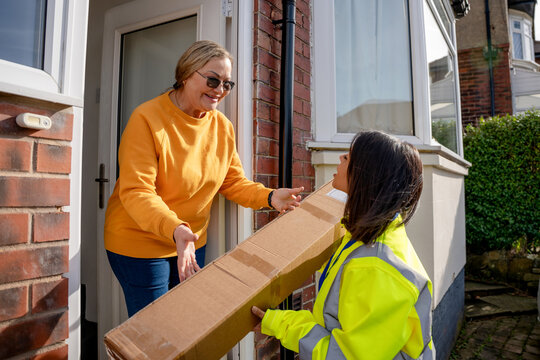 Delivery person hands package to resident at home entrance during daytime
