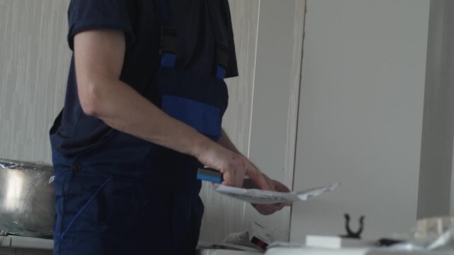 Close-up of a worker in blue overalls studying a technical manual. Professional furniture assembler checking drawings during kitchen installation