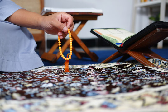 Close-up photo of hands doing dhikr using prayer beads with the Koran on the background as a background. Hands are praying. A man performs dhikr while holding prayer beads. A Muslim's worship activity