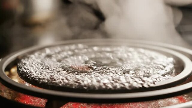 Close-up of melting ice on a stovetop with steam rising, showcasing intricate patterns and textures on a black surface