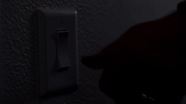 Close up of a human hand switching off a light toggle in a dark room