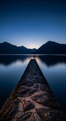 Fototapeta premium Serene stone pier leading to distant mountains across calm lake at twilight blue hour peaceful nature landscape