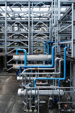 Industrial facility with complex piping and metal framework. Blue and silver pipes run through steel structures. Scene shows heavy machinery and construction details. Image fits engineering