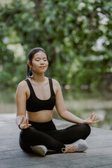 Asian woman meditates outdoors, practicing mindfulness on a lake the forest by nature. Peaceful demeanor highlights a harmonious connection with the tranquil environment.