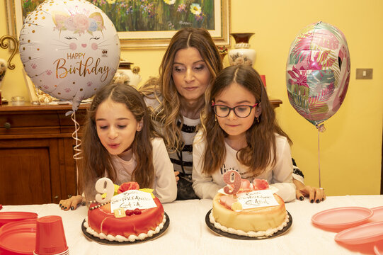 Ritratto di una giovane mamma con le figlie gemelle davanti a due torte il giorno del loro compleanno mentre spengono le candeline.