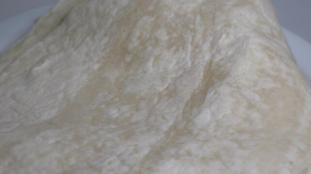 Close-up of a stack of fresh, thin flour tortillas or flatbreads on a white plate, captured on a rotating surface against a neutral background.