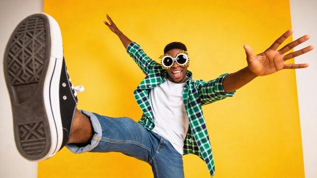 Energetic young man jumping in stylish casual outfit on vibrant yellow background.