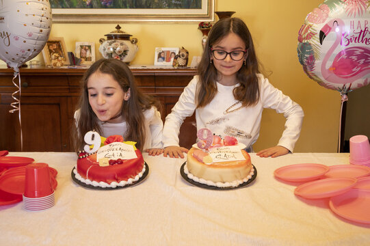 Sorelle gemelle di nove anni mentre spengono le candeline delle torte il giorno del loro compleanno.
