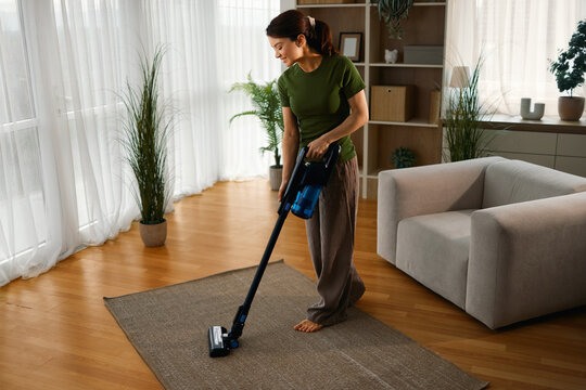 Woman cleaning house carpet with a wireless stick vacuum cleaner