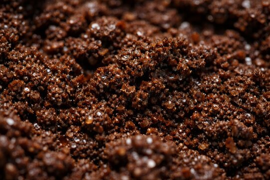 Close up view capturing macro detail of wet dark brown coffee grounds, portraying rich texture and tiny moisture droplets suitable for a conceptual background