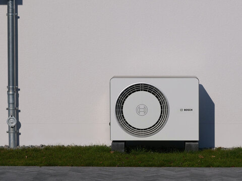 Germany, Paderborn, March 22. 2026, Bosch air-to-water heat pump in front of a white house wall, copy and text space