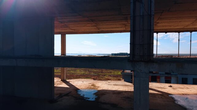 Going up along the open empty floors of the building frame. Approaching the roof of the construction with metal rebars sticking out. Revealing view on the vast seascape in the backdrop.