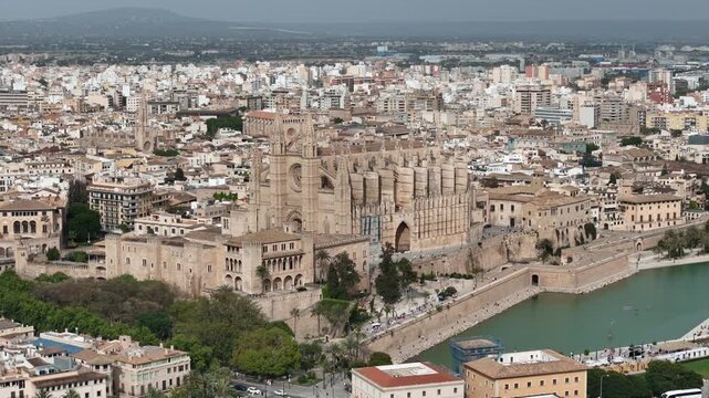 Aerial drone footage of Palma Cathedral (La Seu) and Almudaina Palace overlooking Parc de la Mar in Palma de Mallorca, Spain. Stunning Gothic architecture, historic old town, and Mediterranean coastli