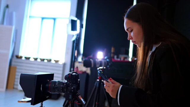 Brunette Caucasian woman holds her phone taking video. Lady is recording video from camera display. Work behind the scenes.