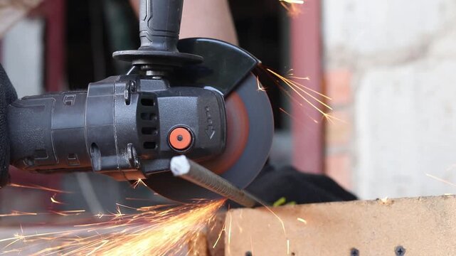 Cordless angle grinder cuts rebar. Sparks fly when cutting rebar with a grinder, construction work close-up. Electric tool for construction and repair work. Grinding machine with metal disc