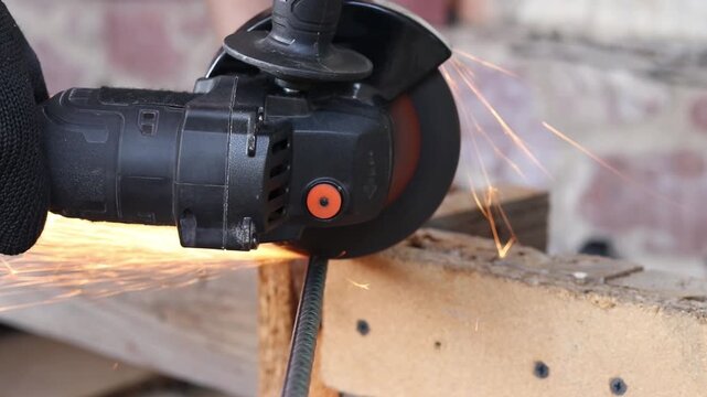 Cordless angle grinder cuts rebar. Sparks fly when cutting rebar with a grinder, construction work close-up. Electric tool for construction and repair work. Grinding machine with metal disc