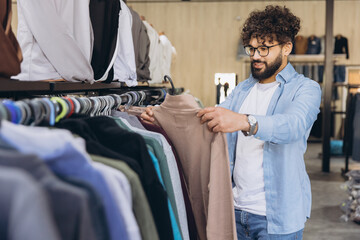 Young Arab man choosing clothing in a boutique, consumer spending for fashionable apparel and...