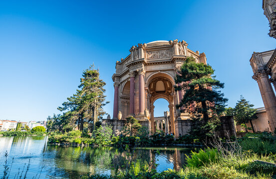 The iconic Palace of Fine Arts rotunda reflects beautifully across the calm lagoon waters on a bright, sunny day in San Francisco, California.