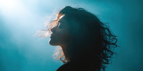 Fototapeta premium Young caucasian female profile silhouette backlit portrait with moody teal rim light and soft atmospheric glow