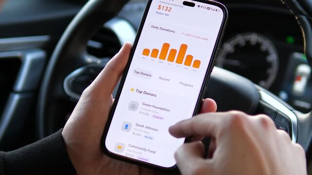 Close-up of hands using a charity fundraising app in a car. Scrolling through donation stats, goals, and top contributors. Highlighting social responsibility and mobile philanthropy. Ideal for non