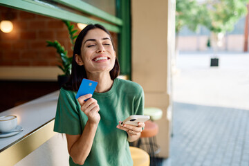 Young woman using credit card for online shopping on her phone drinking coffee in caffee cafeteria