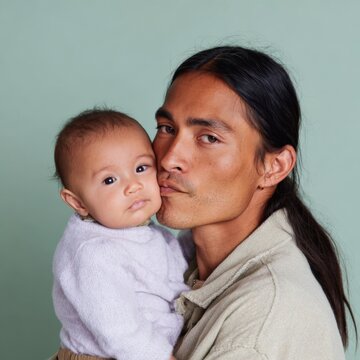 Asian male adult baby newborn father hold embrace direct gaze calm portrait soft green background protective family bond