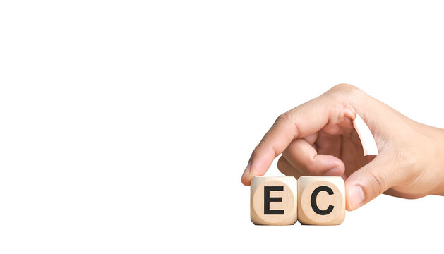 A hand holds two wooden dice showing the letters "E" and "C" against a black backdrop