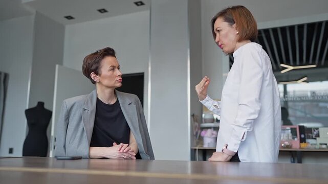 Two women discussing standing by table with wood slat divider in contemporary open office. Discussing, standing, divider, office, teamwork, women.