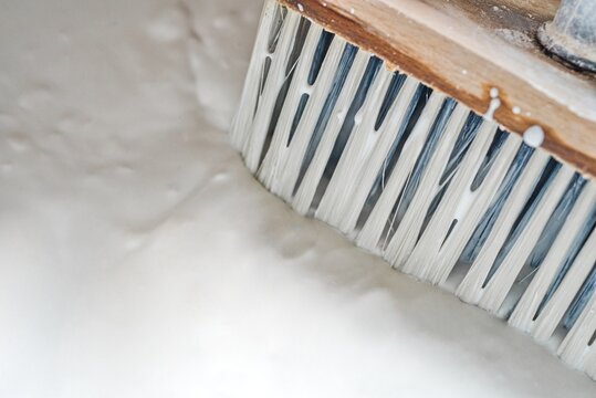Traditional application of white limewash on a wall with a large brush