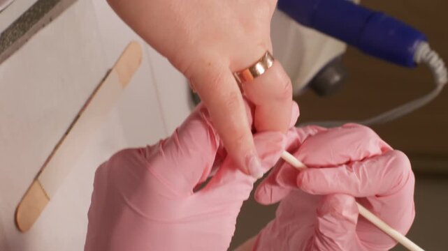 Vertical video. Gel nails. Professional manicure procedure. Woman manicurist hands making hardware machine to beauty client using wooden stick to push back cuticle.