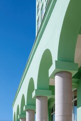Naklejka premium Mint green classical building facade with arched colonnade and stone columns under clear blue sky, vertical perspective emphasizing repeating arches and minimalist architectural details