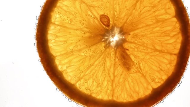 Macro orange slice floating on sparkling liquid surface with bubbles on white background. Fresh citrus texture with light through juicy pulp, ideal for beverage, summer, refreshment and healthy food.