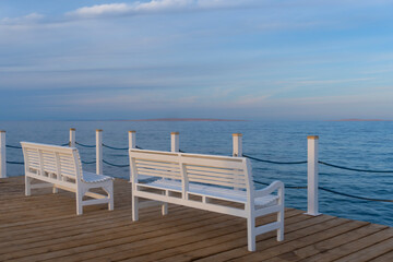 Obraz premium Wooden white benches at the pier with the view of blue sea, cloud beautiful sky