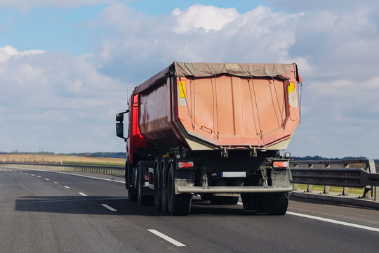 Heavy dump truck driving on highway. Cargo transport vehicle on road in rural landscape. Logistics delivery concept and freight transportation industry with large commercial vehicle in motion.