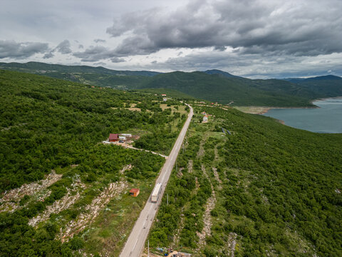 Bosnia and Herzegovina Vlahinja - 05 29 2025 Drone photo of rural Vlahinja, Bosnia showing rolling green hills, paved road leading to Montenegro, Bileća Lake, and distant Gradac mountains under cloudy