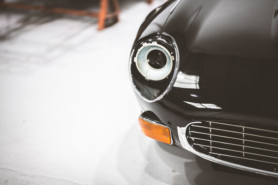 Close-up of a classic black car's front headlight and grille in a workshop setting