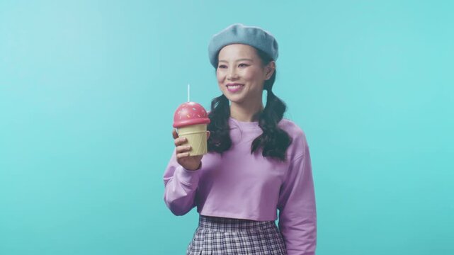 Elegant woman with beret enjoying refreshing beverage against vibrant blue backdrop in studio setting