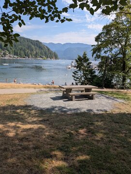 A beautiful day in the park. An empty bench with a beautiful sea view through trees. Panoramic view of the Deep Cove Beach in North Vancouver