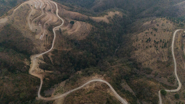 Top-down aerial view near Dwara village, Dehradun, Uttarakhand, showing a dirt path along a mountain ridge with terrace farms and misty forested slopes on a winter evening.
