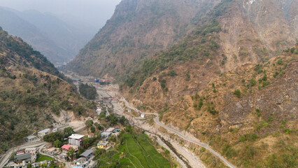 Fototapeta premium Aerial view of the Song River in Maldevta near Dehradun, Uttarakhand, showing low water flow in winter with a village house, greenery, and dirt roads across the mountain landscape.