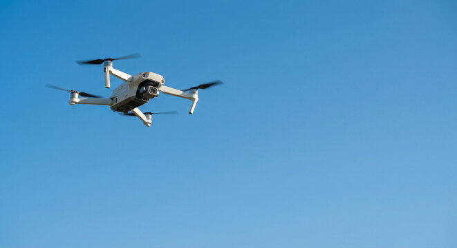 Aerial view of a modern white quadcopter drone with camera flying in clear blue sky during daytime, professional UAV for aerial photography and videography